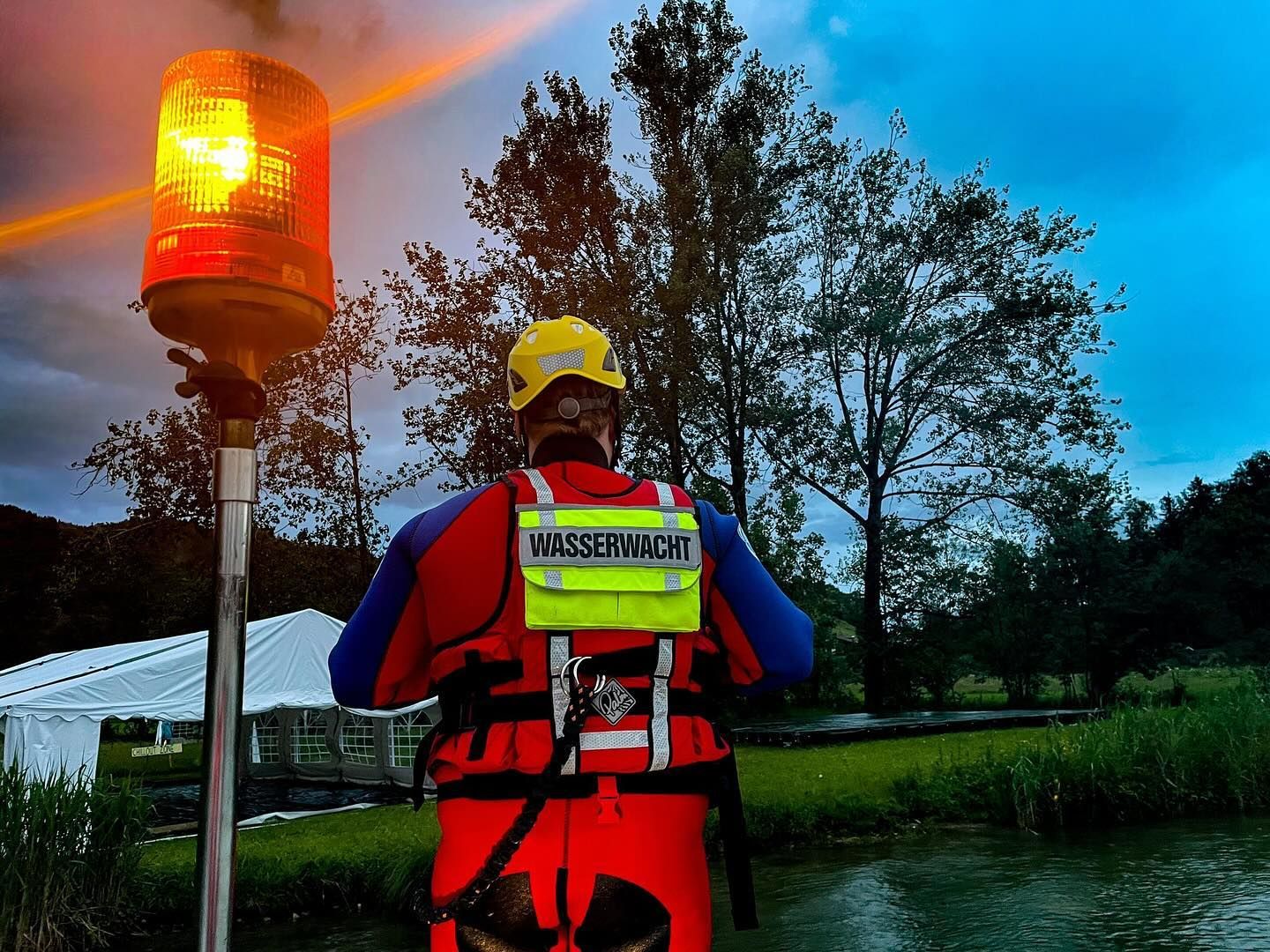 Ein Rettungsschwimmer im Wasserrettungsdienst steht neben einer orangenen Einsatzleuchte auf dem Boot im See