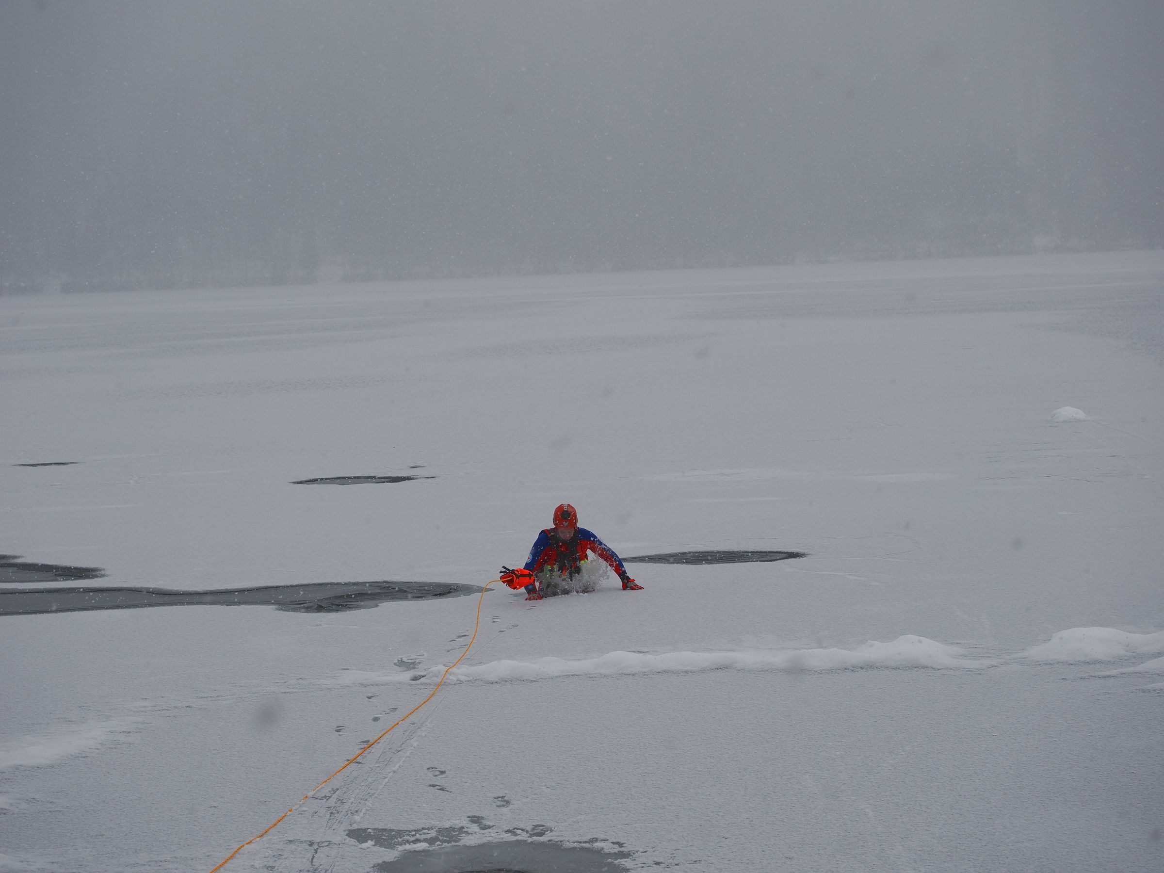 Um die nicht vorhandene Tragfähigkeit des zugefrorenen Schliersees der Presse vorzuführen bricht ein Jugendmitglied in Schutzkleidung ins Eis ein