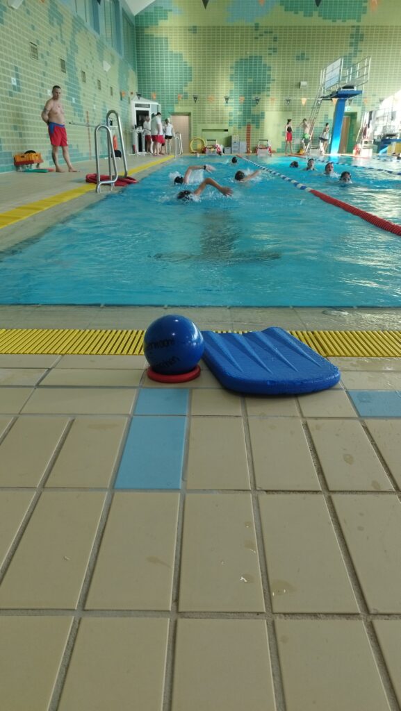 Kinder schwimmen sich im Schwimmbad Bad Tölz ein. Am Beckenrand liegen Schwimmutensilien